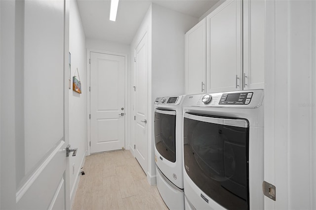 laundry room with cabinets, light wood-type flooring, and washer and clothes dryer