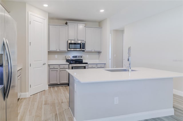 kitchen with an island with sink, light wood-style flooring, a sink, appliances with stainless steel finishes, and light countertops