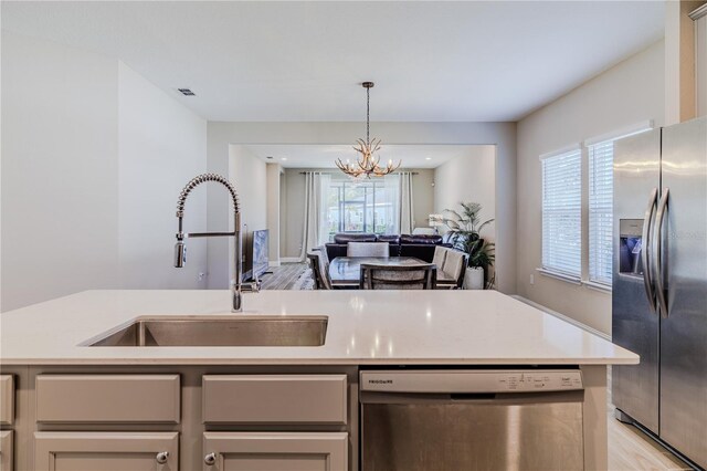 kitchen with appliances with stainless steel finishes, open floor plan, decorative light fixtures, light countertops, and a sink