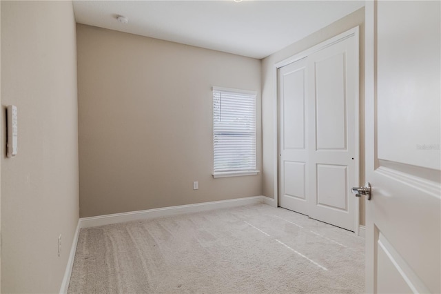 unfurnished bedroom with a closet, light colored carpet, and baseboards