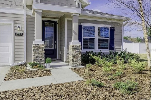 property entrance with an attached garage, stone siding, and fence