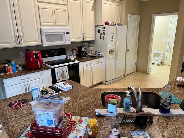 kitchen with tasteful backsplash, white cabinets, dark stone counters, light tile patterned floors, and white appliances