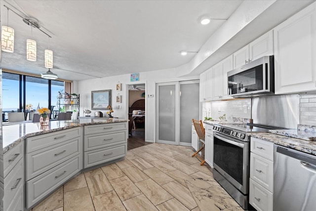 kitchen featuring appliances with stainless steel finishes, white cabinetry, backsplash, hanging light fixtures, and light stone counters