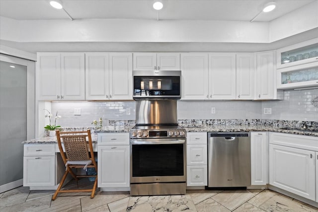 kitchen featuring light stone countertops, decorative backsplash, stainless steel appliances, and white cabinets