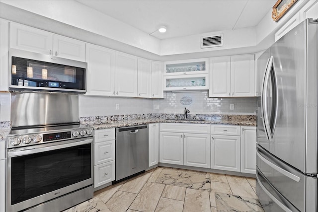 kitchen featuring sink, white cabinetry, light stone counters, appliances with stainless steel finishes, and backsplash