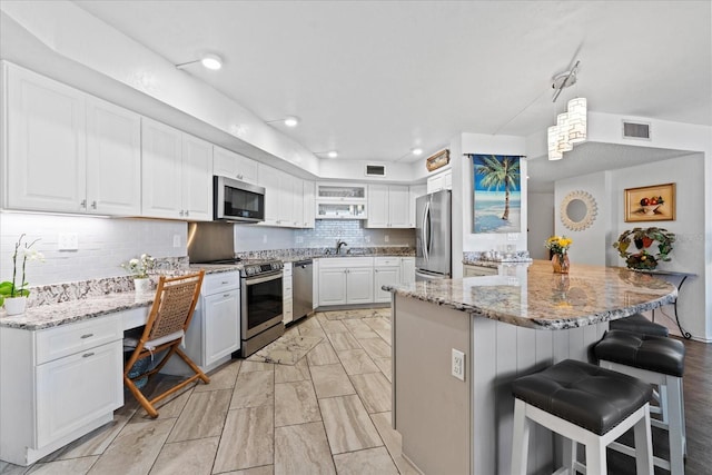 kitchen with appliances with stainless steel finishes, a breakfast bar, white cabinetry, hanging light fixtures, and light stone counters