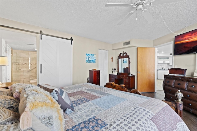 bedroom with ensuite bathroom, a barn door, dark hardwood / wood-style floors, and a textured ceiling