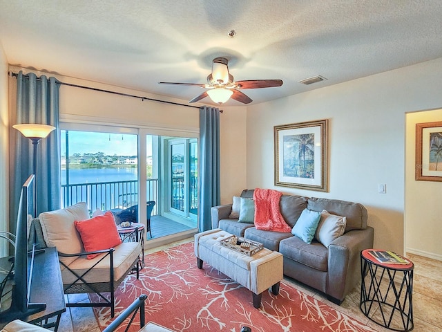 living room with ceiling fan, a textured ceiling, and a water view