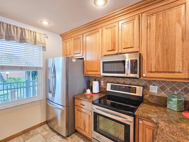 kitchen featuring light tile patterned flooring, appliances with stainless steel finishes, tasteful backsplash, dark stone counters, and a textured ceiling