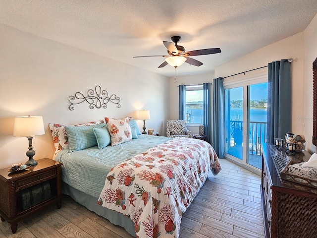 bedroom featuring ceiling fan, access to exterior, a water view, light hardwood / wood-style floors, and a textured ceiling