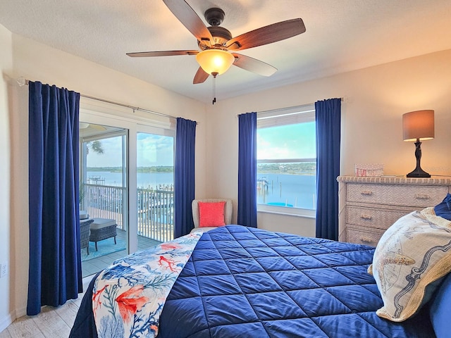 bedroom featuring hardwood / wood-style flooring, access to outside, ceiling fan, a water view, and a textured ceiling