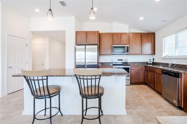 kitchen featuring sink, a kitchen island, stainless steel appliances, a kitchen bar, and decorative light fixtures