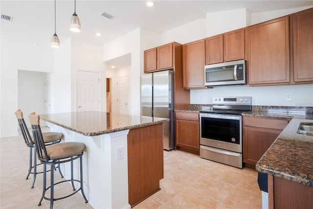 kitchen featuring a kitchen bar, decorative light fixtures, a center island, dark stone counters, and stainless steel appliances