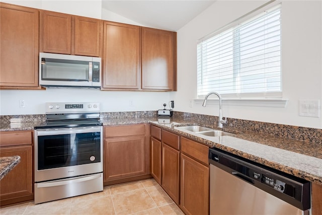 kitchen featuring appliances with stainless steel finishes, lofted ceiling, sink, dark stone countertops, and light tile patterned floors