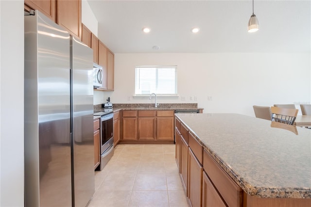 kitchen with sink, a kitchen island, stainless steel appliances, light tile patterned flooring, and decorative light fixtures