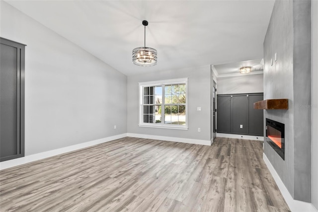 unfurnished living room with vaulted ceiling, a large fireplace, a notable chandelier, and light hardwood / wood-style floors