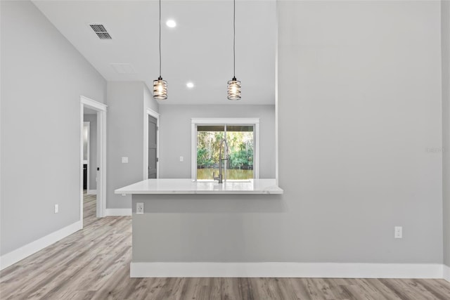 kitchen featuring hanging light fixtures, sink, light hardwood / wood-style flooring, and kitchen peninsula