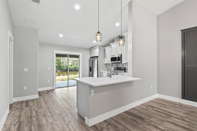 kitchen with appliances with stainless steel finishes, pendant lighting, white cabinets, backsplash, and kitchen peninsula