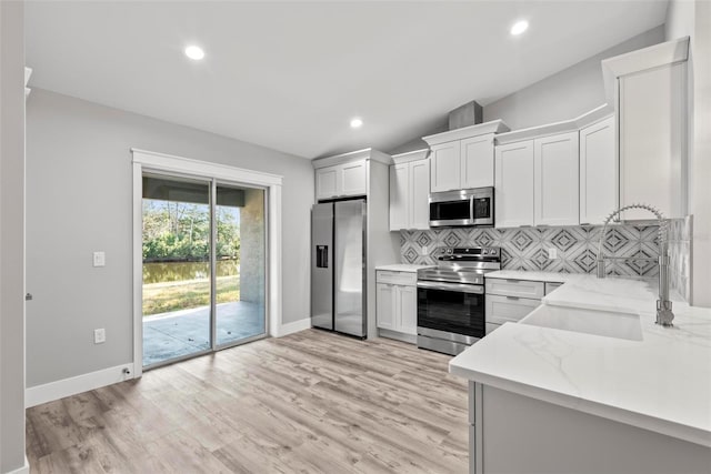 kitchen featuring white cabinetry, stainless steel appliances, light stone counters, tasteful backsplash, and light wood-type flooring