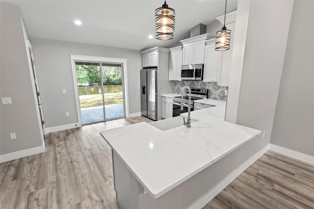 kitchen featuring pendant lighting, appliances with stainless steel finishes, tasteful backsplash, white cabinets, and kitchen peninsula