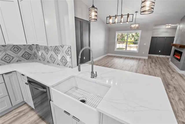 kitchen with sink, tasteful backsplash, light stone counters, dishwasher, and pendant lighting