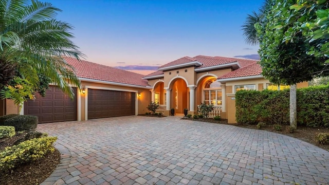 mediterranean / spanish-style home featuring a tiled roof, decorative driveway, an attached garage, and stucco siding