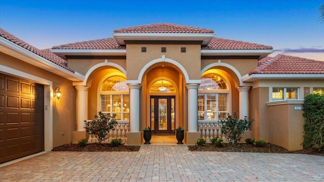 property entrance featuring a tile roof, an attached garage, and stucco siding