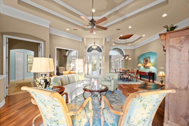 interior space with arched walkways, ceiling fan with notable chandelier, wood finished floors, ornamental molding, and a tray ceiling