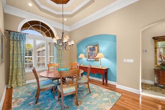 dining room featuring baseboards, wood finished floors, an inviting chandelier, a tray ceiling, and crown molding