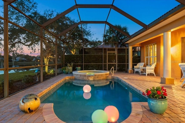 pool at dusk featuring glass enclosure, a pool with connected hot tub, and a patio