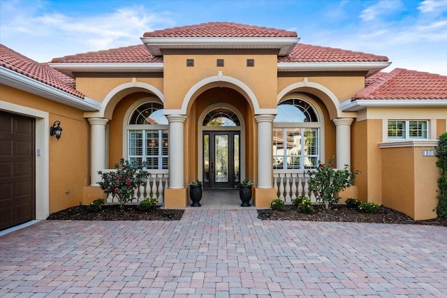 entrance to property featuring an attached garage, covered porch, a tiled roof, and stucco siding