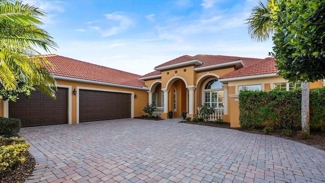 mediterranean / spanish-style house with an attached garage, a tile roof, decorative driveway, and stucco siding