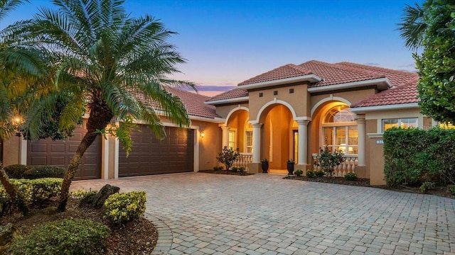 mediterranean / spanish house featuring a garage, decorative driveway, a tiled roof, and stucco siding