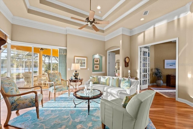 interior space with a raised ceiling, visible vents, crown molding, and wood finished floors