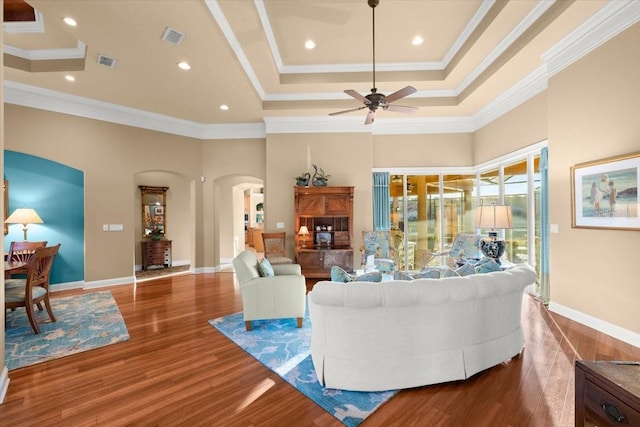 living area with visible vents, arched walkways, wood finished floors, and ornamental molding