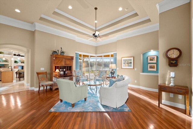 living room with ceiling fan, a raised ceiling, and wood finished floors