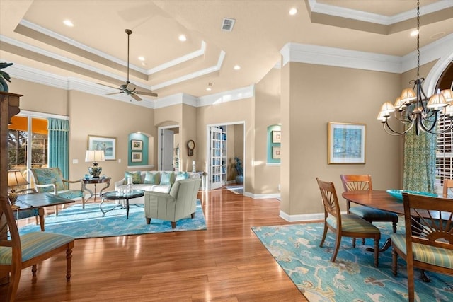 interior space featuring baseboards, arched walkways, wood finished floors, a tray ceiling, and ceiling fan with notable chandelier