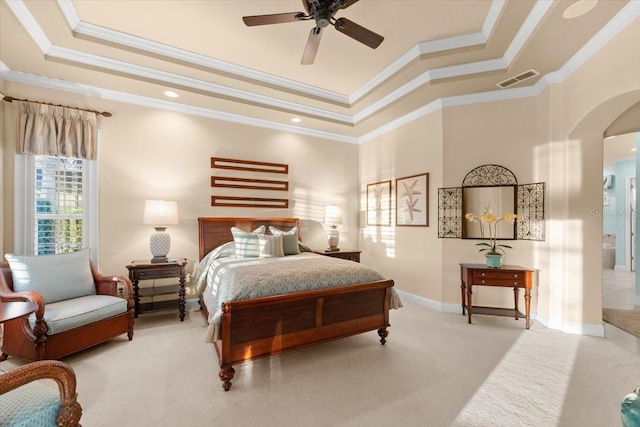 carpeted bedroom with baseboards, visible vents, arched walkways, a tray ceiling, and crown molding