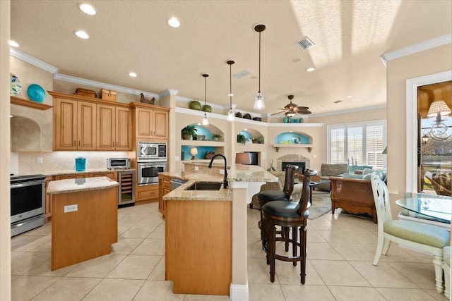 kitchen featuring wine cooler, a sink, visible vents, appliances with stainless steel finishes, and a center island with sink