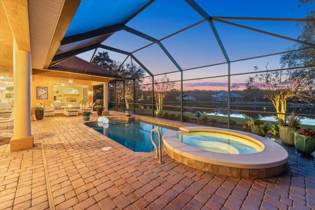 pool at dusk featuring a pool with connected hot tub, a patio area, outdoor lounge area, and a lanai