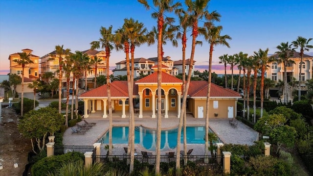 pool at dusk with fence private yard, a patio area, a residential view, and a community pool