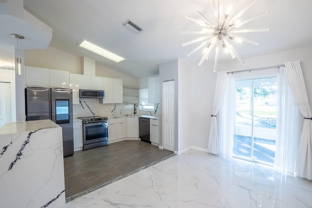 kitchen with appliances with stainless steel finishes, white cabinetry, light stone counters, vaulted ceiling, and a chandelier