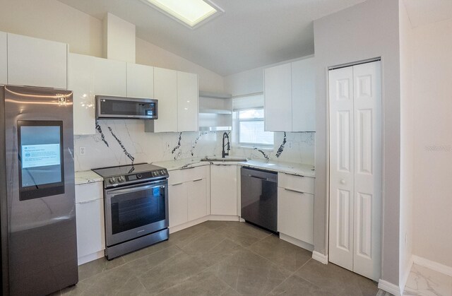 kitchen with vaulted ceiling, appliances with stainless steel finishes, white cabinetry, sink, and decorative backsplash