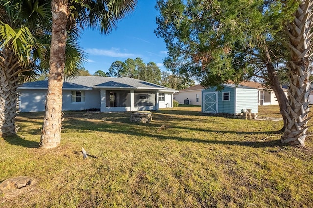 rear view of property featuring a shed, a lawn, and an outdoor fire pit