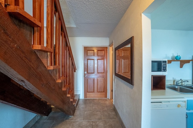 hallway featuring a sink, a textured ceiling, dark tile patterned flooring, baseboards, and stairs