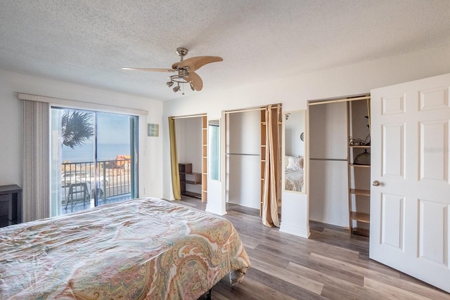 bedroom featuring a textured ceiling, a ceiling fan, multiple closets, access to outside, and light wood finished floors