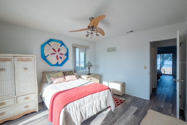 bedroom featuring a textured ceiling, dark wood-style flooring, a ceiling fan, visible vents, and baseboards