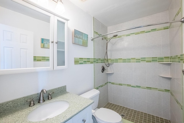 bathroom with toilet, a tile shower, and vanity