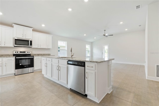 kitchen featuring sink, appliances with stainless steel finishes, white cabinetry, light stone counters, and an island with sink