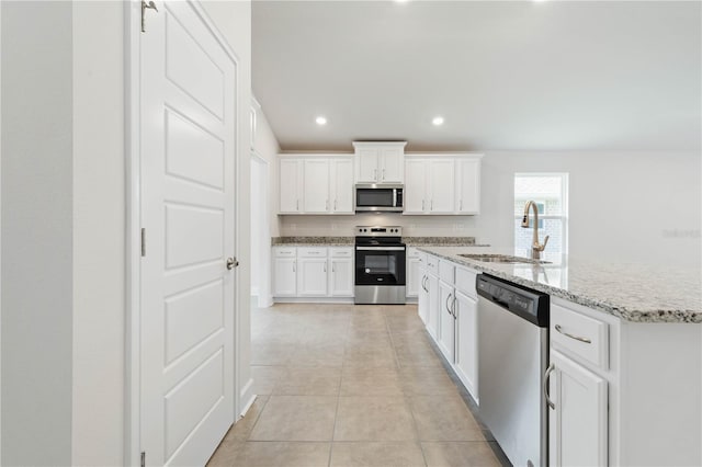 kitchen with sink, light tile patterned floors, stainless steel appliances, light stone counters, and white cabinets